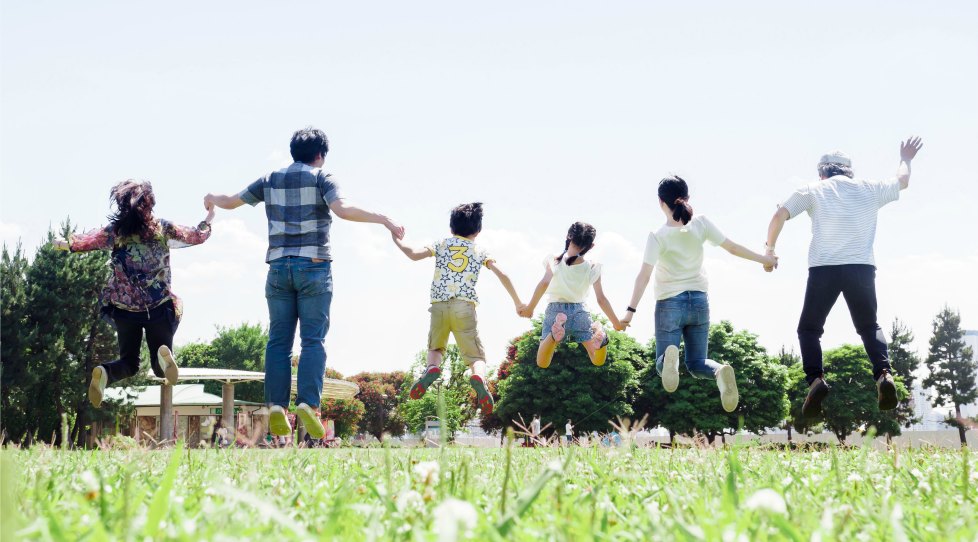原っぱで横一列に手をつないで、ジャンプする家族の後ろ姿
