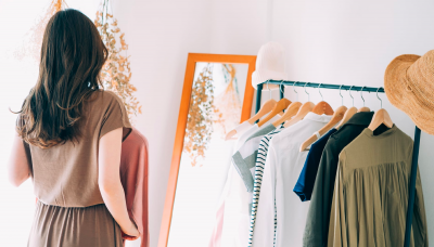 鏡の前で服を選ぶ女性の後ろ姿とハンガーに掛けられた服