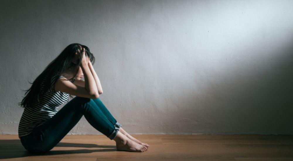 薄暗い部屋にうずくまって頭を抱える女性に一筋の光が当たる